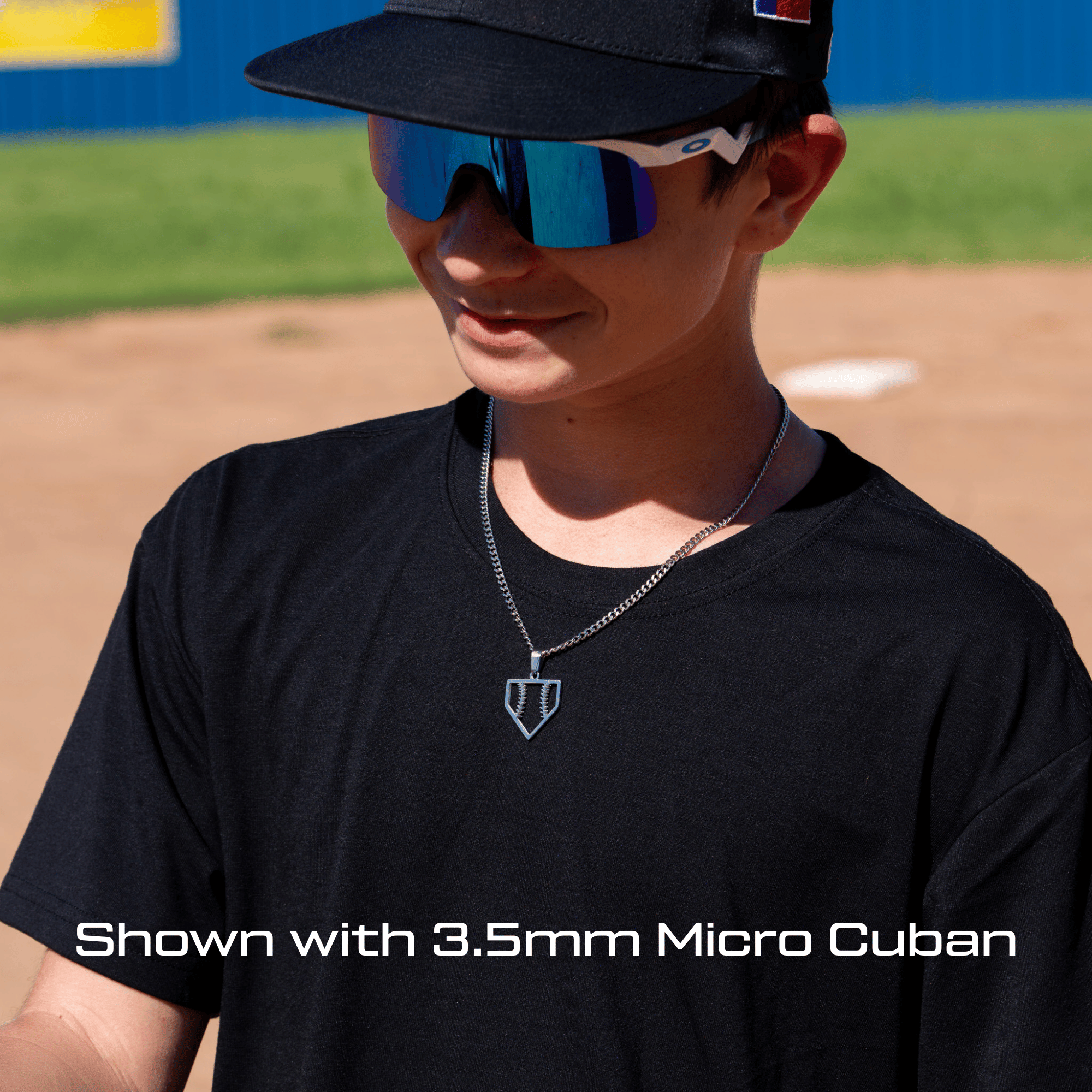 Person wearing a black cap and sunglasses on a baseball field wearing the all in faith home plate baseball necklace