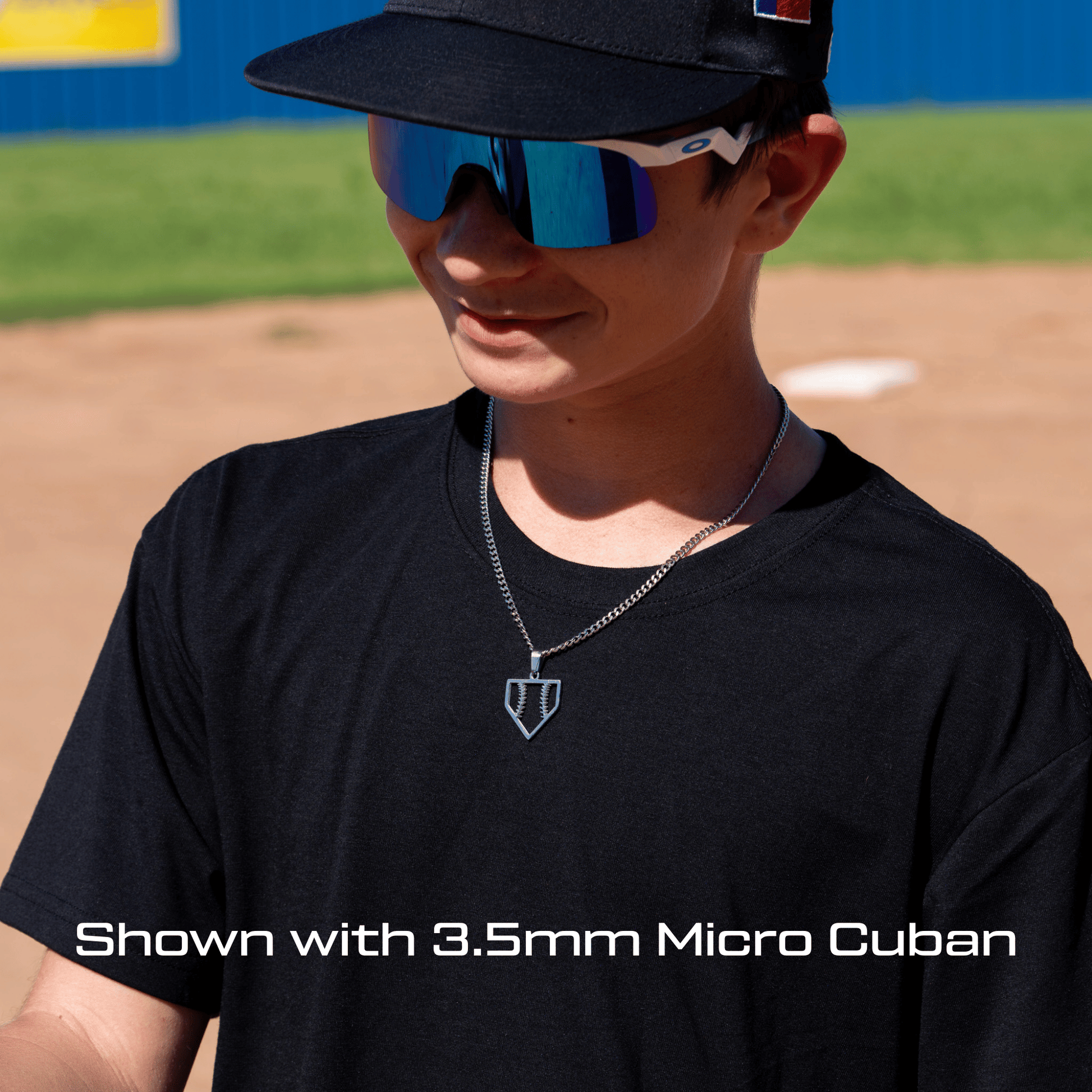 Person wearing a black cap and sunglasses on a baseball field wearing the all in faith home plate baseball necklace