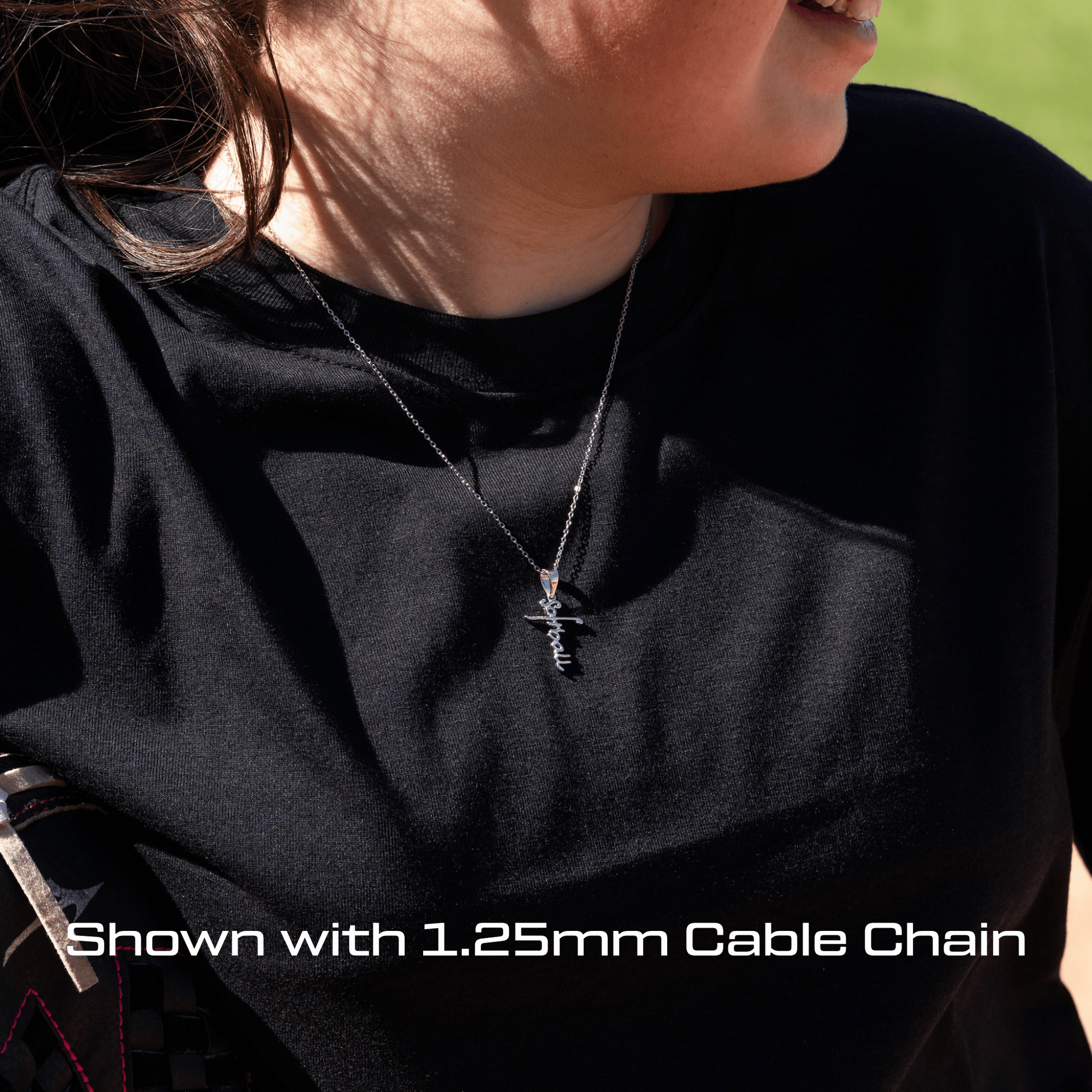 Person wearing a black shirt with a necklace featuring an all in faith softball script cross necklace