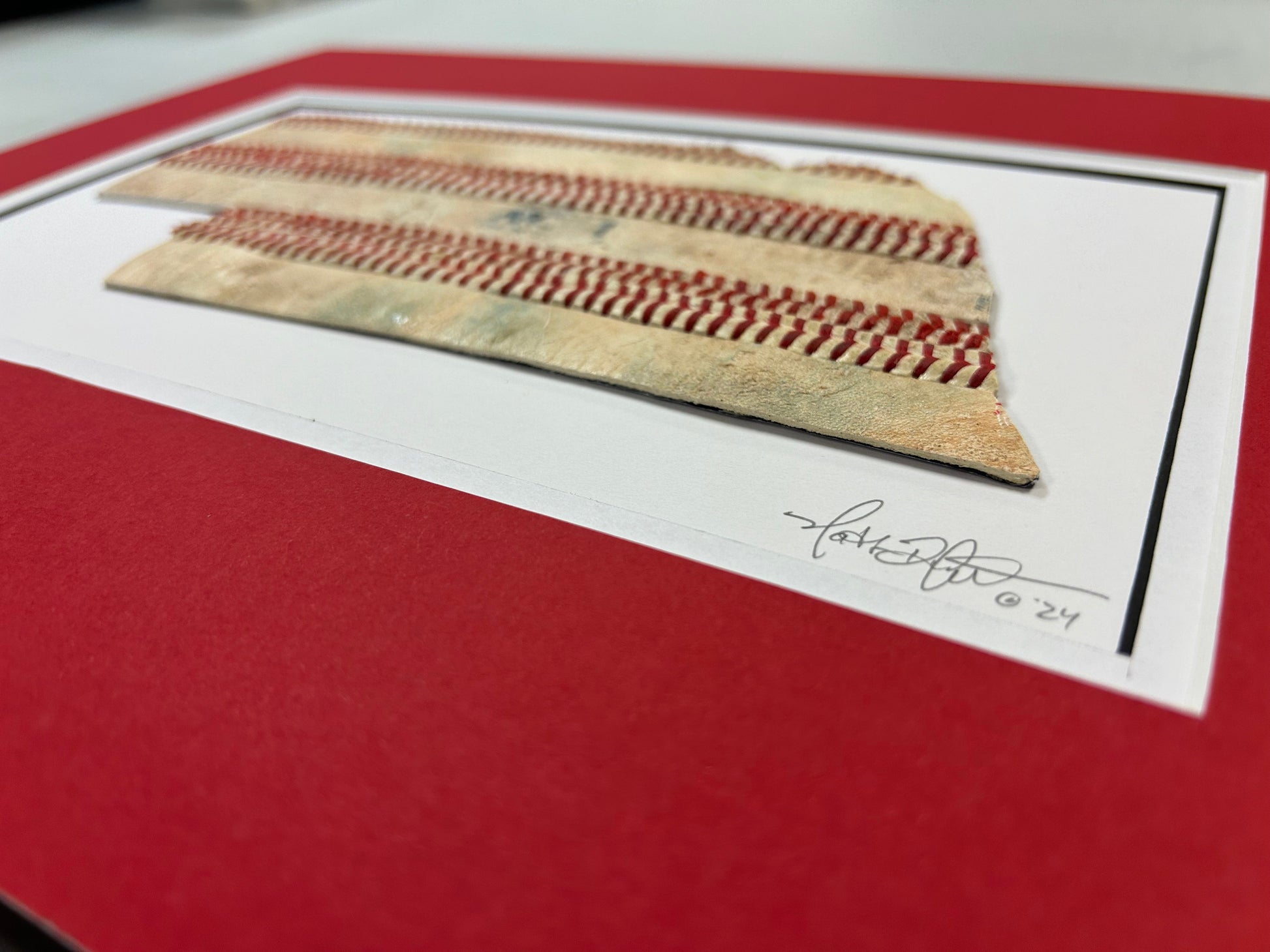 Nebraska Baseball Artwork - Made from Reclaimed Baseballs displayed on a red matting, showcasing the unique texture of baseballs.