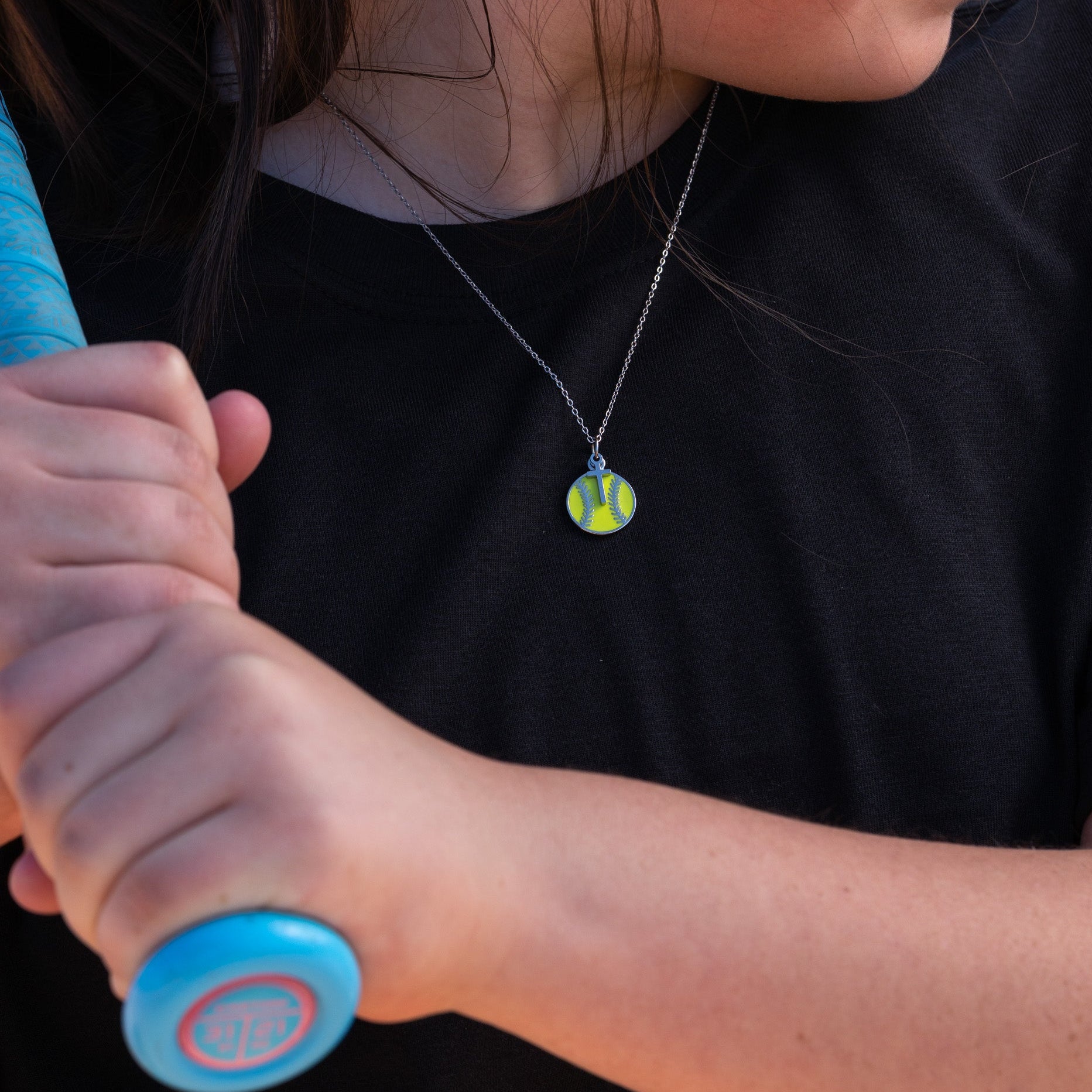 Christian Softball Cross Necklace: Softball player holding a softball bat with a silver necklace featuring a softball with a dangling cross