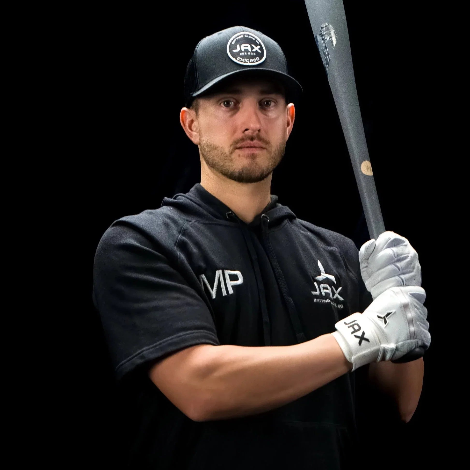 Jax Athletics Platinum White Baseball Gloves | Pro Cuff | Man holding a baseball bat wearing a black cap, hoodie, and gloves with 'JAX' branding on a black background.