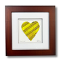 Softball Heart Artwork titled “Seams of Love” featuring a handcrafted heart design in yellow leather.
