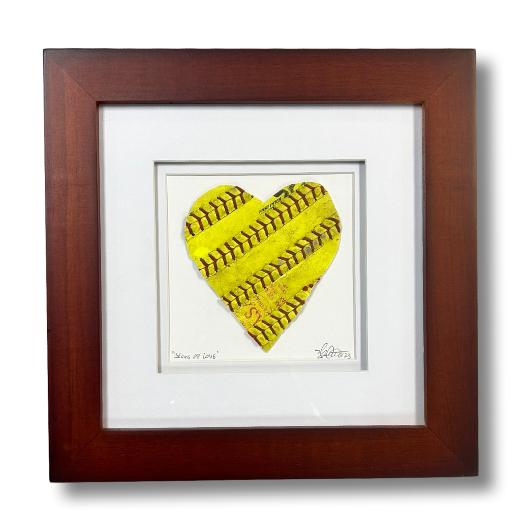 Softball Heart Artwork titled “Seams of Love” featuring a handcrafted heart design in yellow leather.