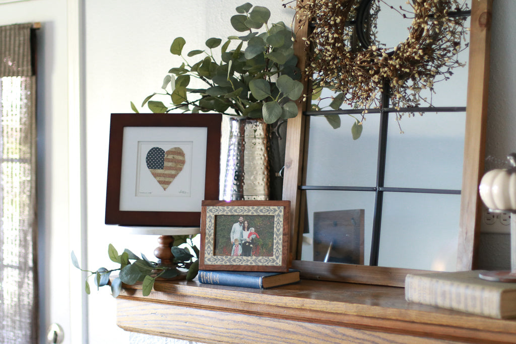 Decorative living room shelf featuring America's Love Original Artwork, framed photos, plants, and a rustic mirror.