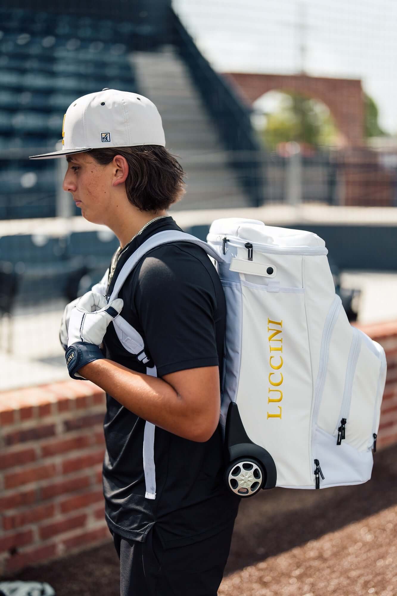Luccini Baseball Wheeled Gear Bag – White | Baseball player wearing a white backpack with 'Lucchini' branding outdoors.
