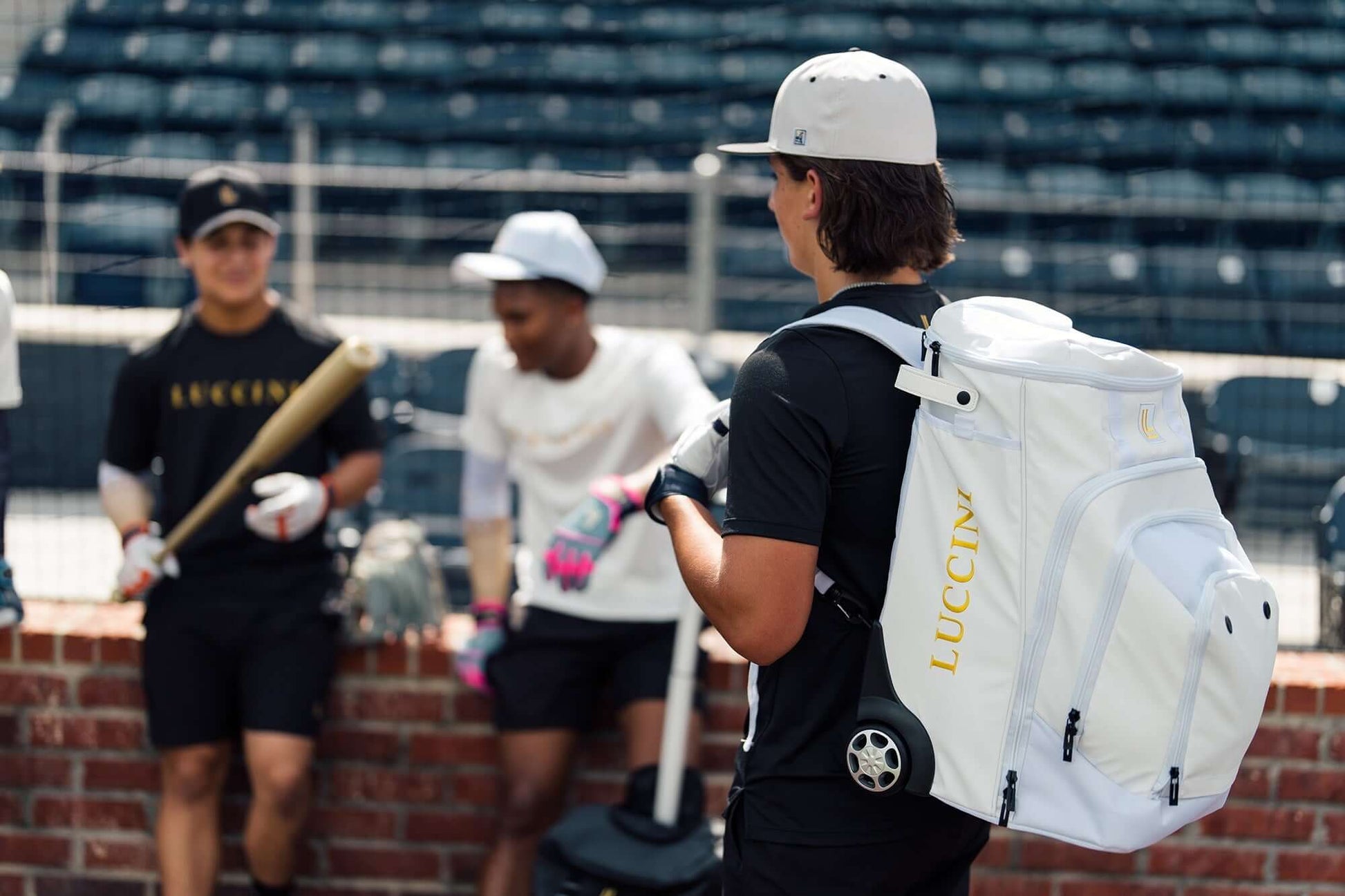 Luccini Baseball Wheeled Gear Bag – White | Baseball player with a white backpack labeled 'Lucchese' at a sports event.
