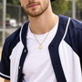 Man wearing all in faith home plate corss neckalce a navy and white varsity jacket with a cap, standing outdoors.