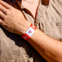 Person wearing a orange wristband with AIF branding on a beige shirt background