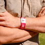 Person wearing a pink wristband with AIF branding on a beige shirt background
