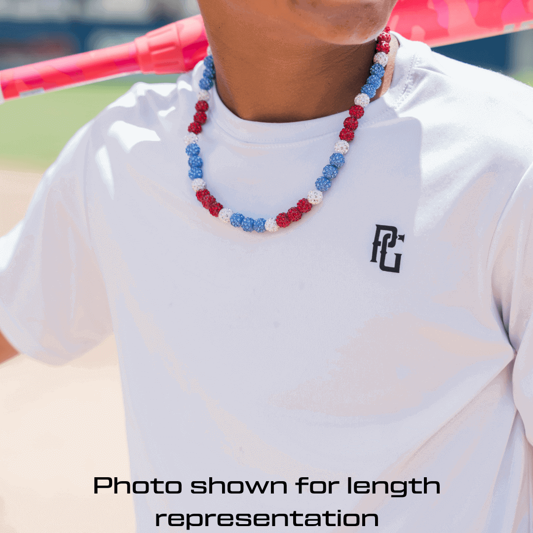 baseball player wearing a white shirt with a logo and a colorful beaded necklace, with a blurred background.