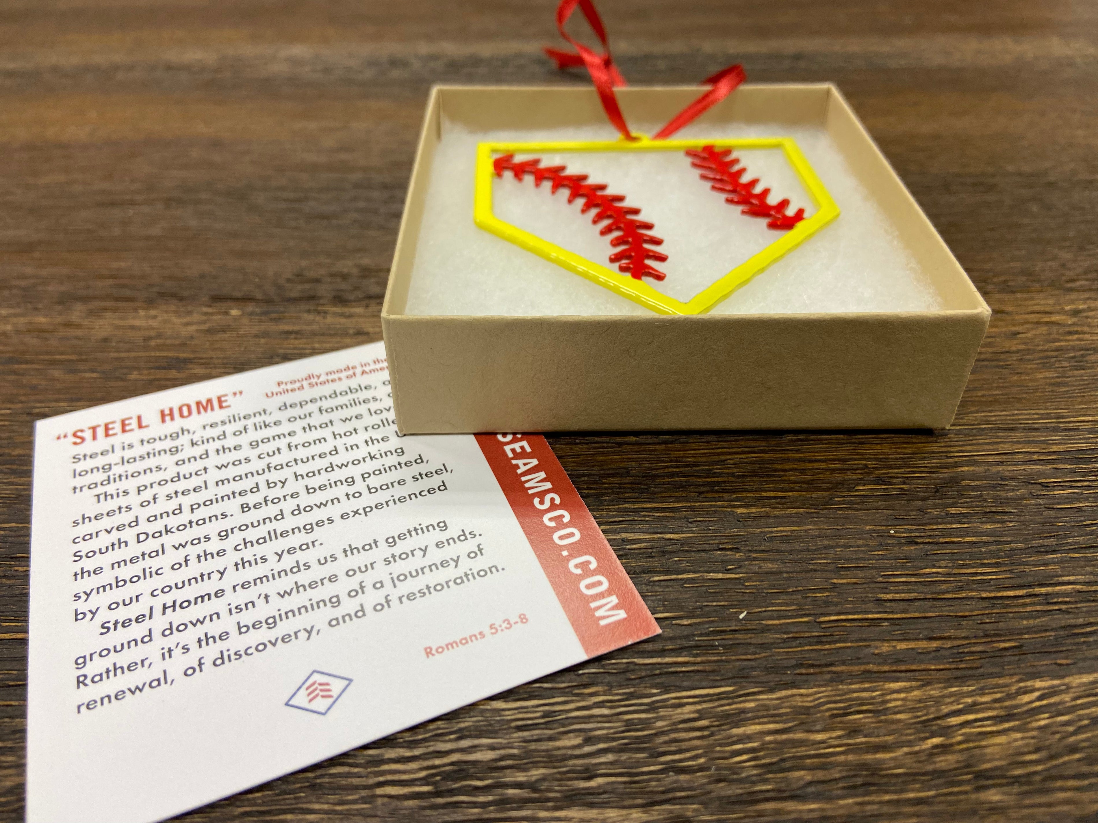 STEEL HOME" Softball Christmas Ornament in a gift box with a red ribbon and informational card.
