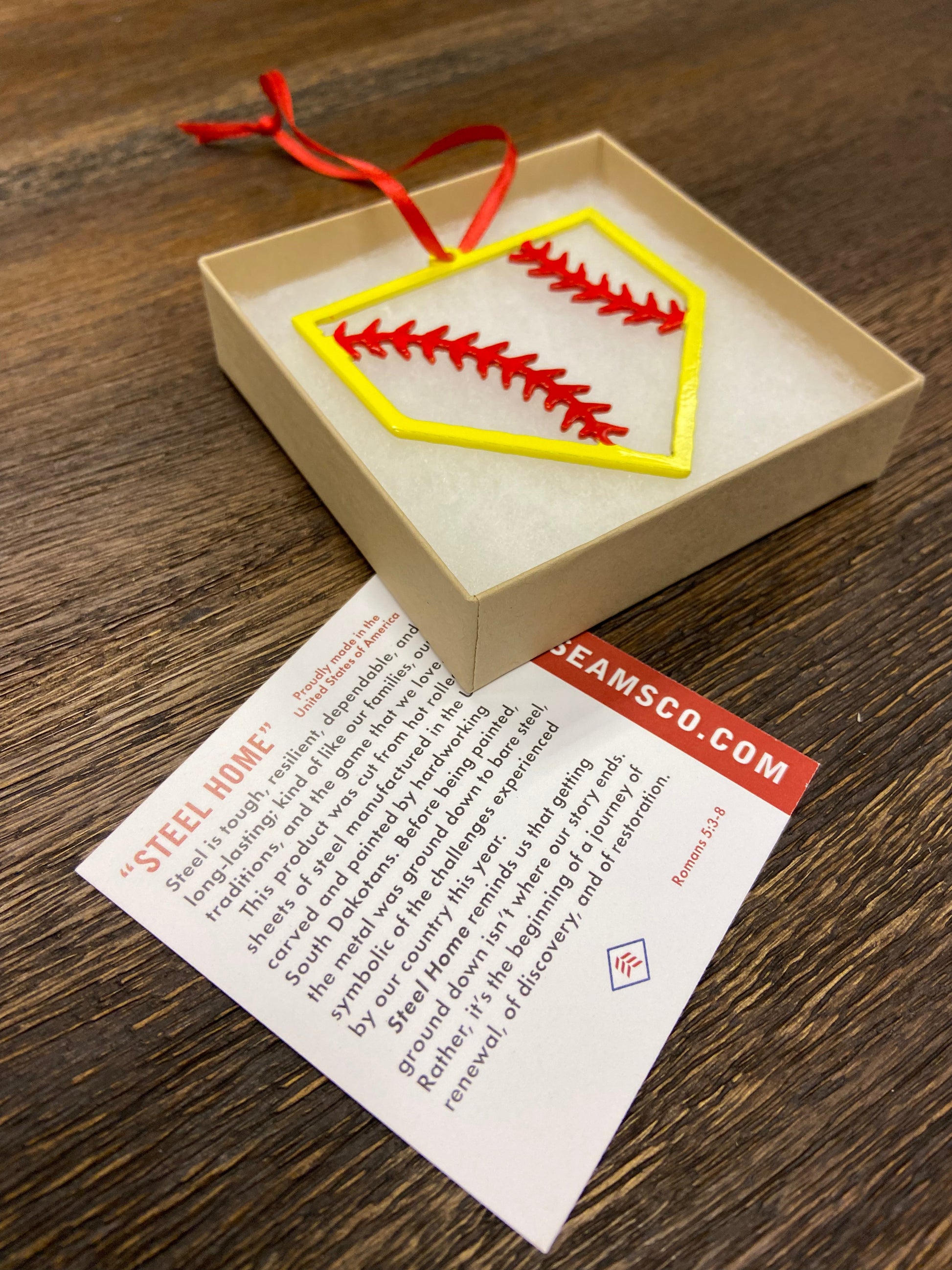 "STEEL HOME" Softball Christmas Ornament displayed in a gift box with a card detailing its origin.