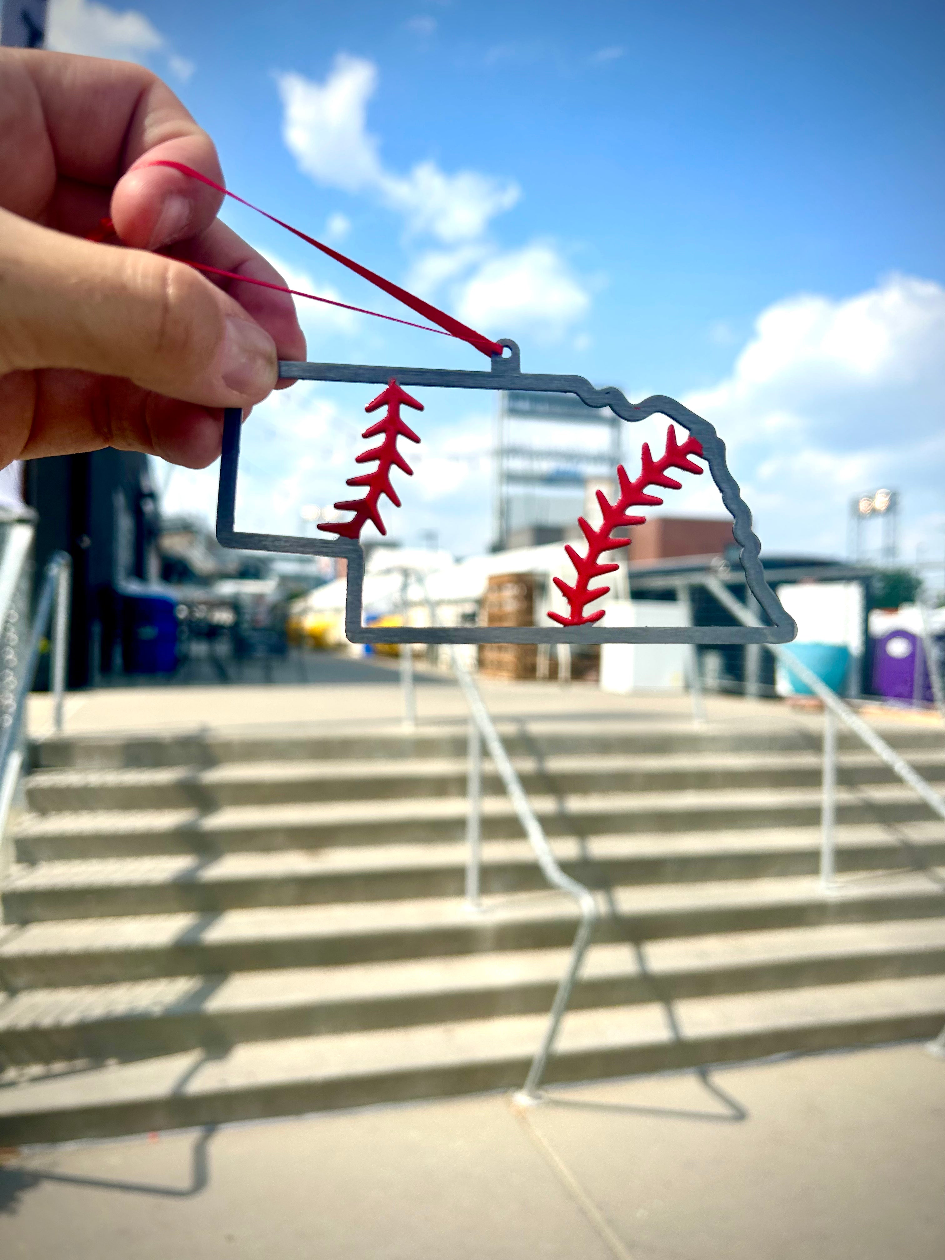 Nebraska Steel Baseball Christmas Ornament held outdoors, showcasing its unique design and vibrant colors.